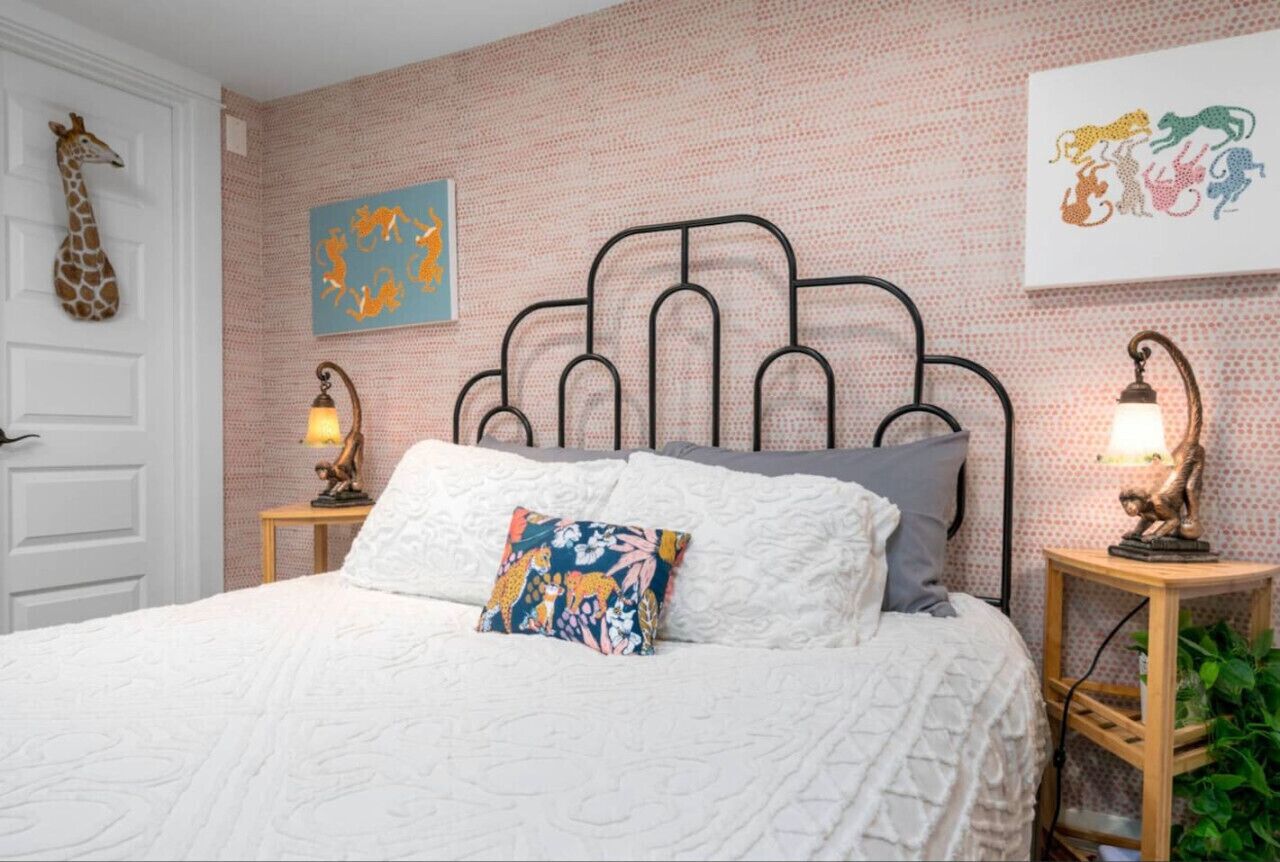 A bedroom with a white bed, a patterned pillow, a giraffe wall decoration, and two wall-mounted lamps.