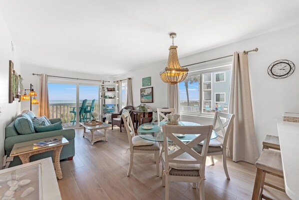 A spacious living area with a view of the sea, a dining table with chairs, and a cozy seating area with a sofa.