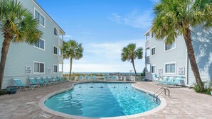 A pool area with a clear view of the ocean, surrounded by two-story buildings with balconies and lounge chairs.