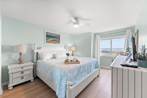 Un dormitorio con cama, mesitas de noche, escritorio, silla, ventana con vistas y ventilador de techo.