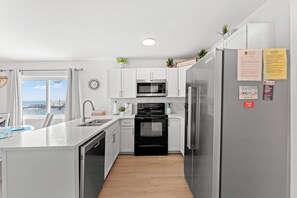 Una cocina moderna con armarios blancos, electrodomésticos de acero inoxidable y vista al océano.