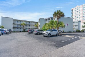 Un estacionamiento con varios coches, un edificio con un letrero que dice "Beach Garden" y una palmera.