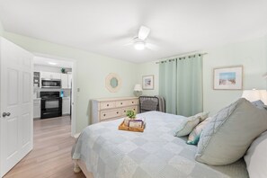A bedroom with a bed, dresser, and a view into the kitchen.