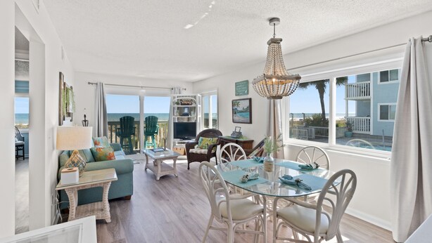 A spacious living area with a glass dining table, wicker furniture, and a view of the ocean.