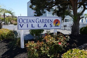 Señal de Ocean Garden Villas con un logotipo, rodeada de jardines y un edificio al fondo.