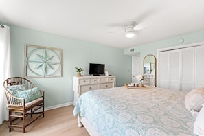 A bedroom with a bed, a chair, a dresser, a television, a ceiling fan, and a large mirror. - Ocean Garden Villas E1-2BR/2BA Oceanfront Condo in Crescent Beach (North Myrtle Beach)