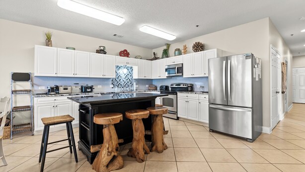 Una cocina moderna con armarios blancos, un refrigerador de acero inoxidable y una isla central con taburetes.