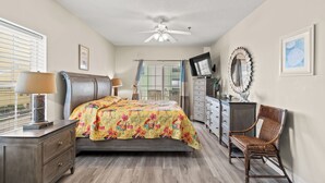 Un dormitorio con cama, cómoda, silla, ventilador de techo y ventana con persianas.