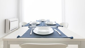 A dining table set with plates, glasses, and cutlery, with a blue placemat and a white chair. - Rivazzurra Homes - 3 (Termoli)