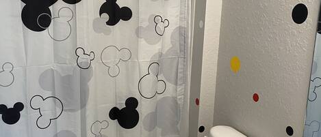 A bathroom with a Mickey Mouse themed shower curtain, a toilet, and a sink.