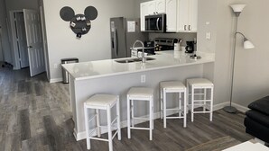 A modern kitchen with a central island, white bar stools, and a Mickey Mouse head decoration on the wall.