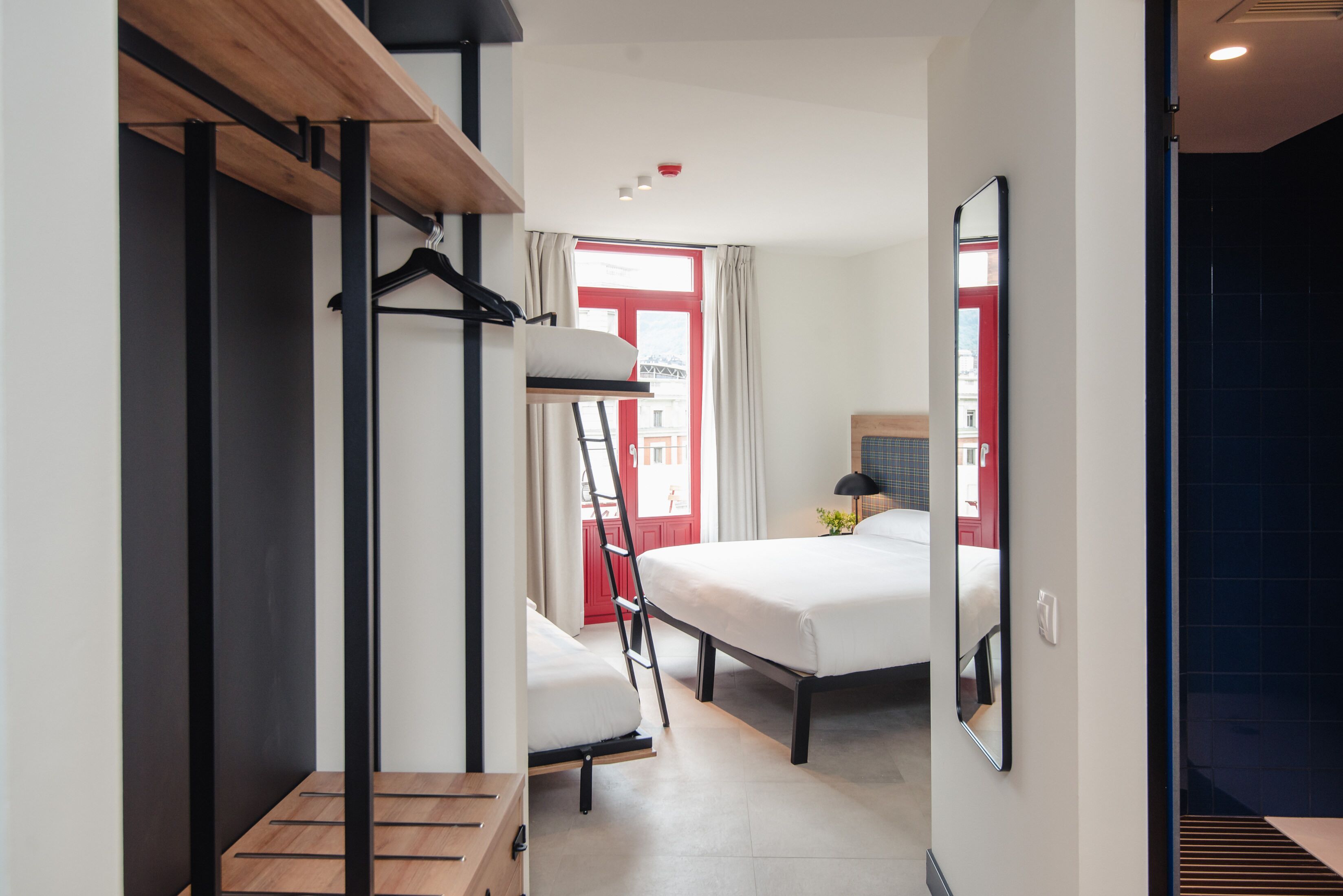 Une chambre d’hôtel de taille réduite, équipée d’un lit superposé, d’un bureau et d’un miroir.