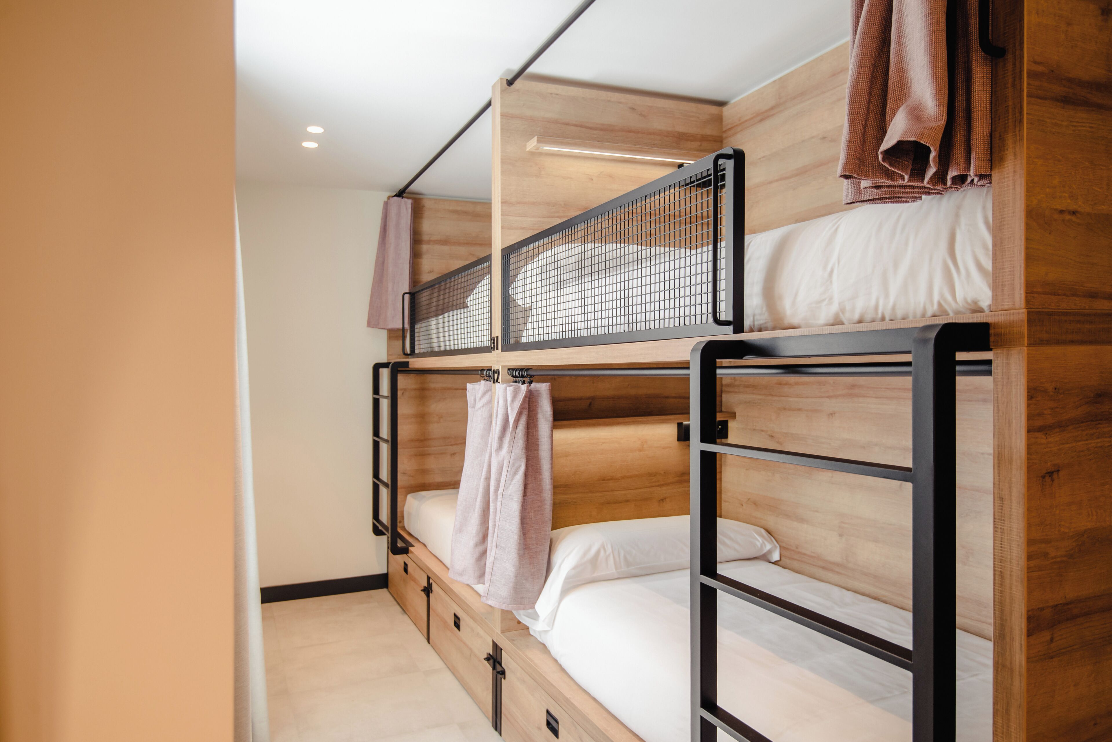 Een slaapkamer met stapelbedden, houten frames, een wit matras en een handdoek.