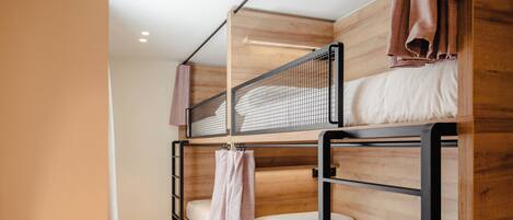 Een slaapkamer met stapelbedden, houten frames, een wit matras en een handdoek.