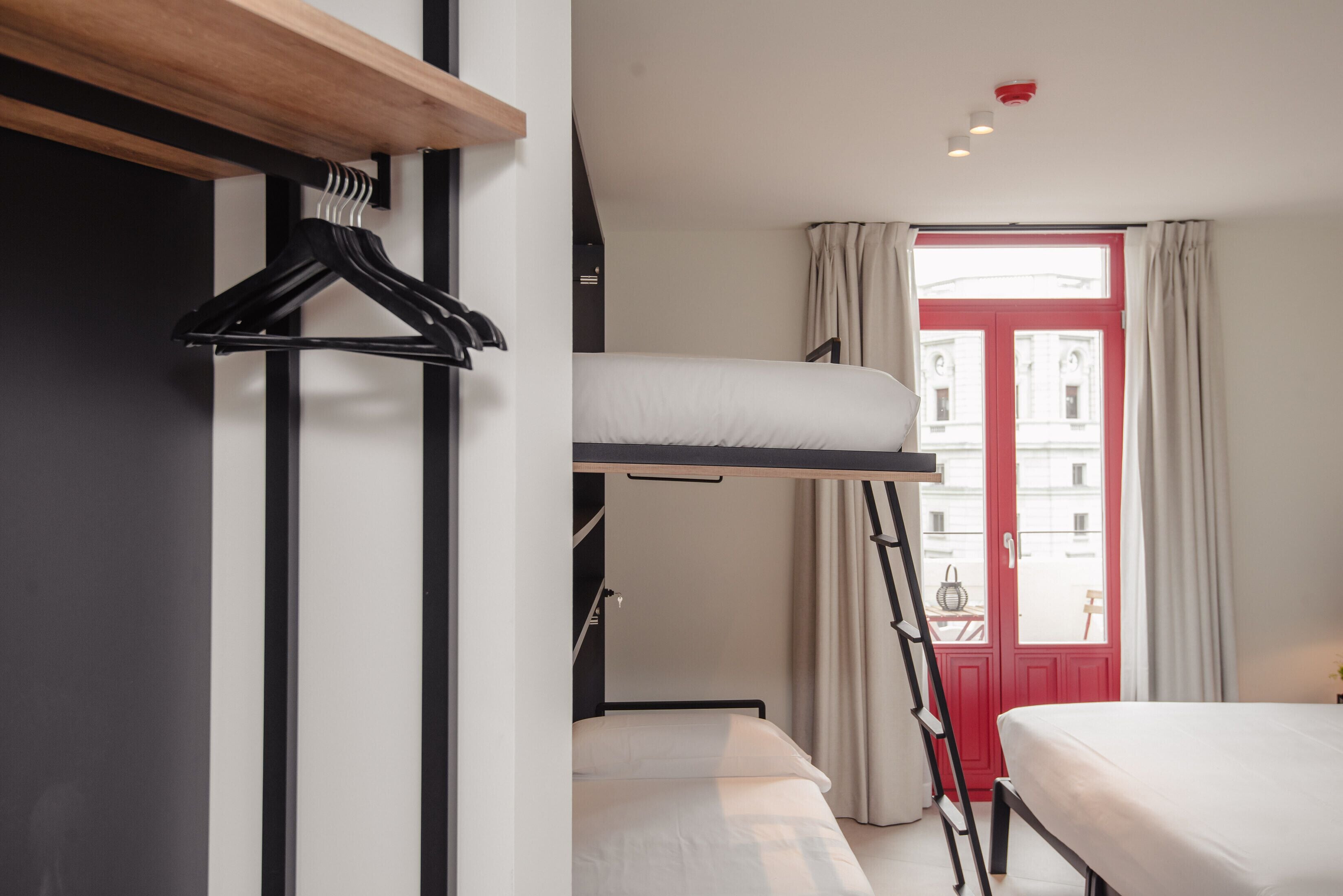 Une chambre avec un lit superposé, une étagère en bois, un porte-manteau et une fenêtre avec des rideaux.