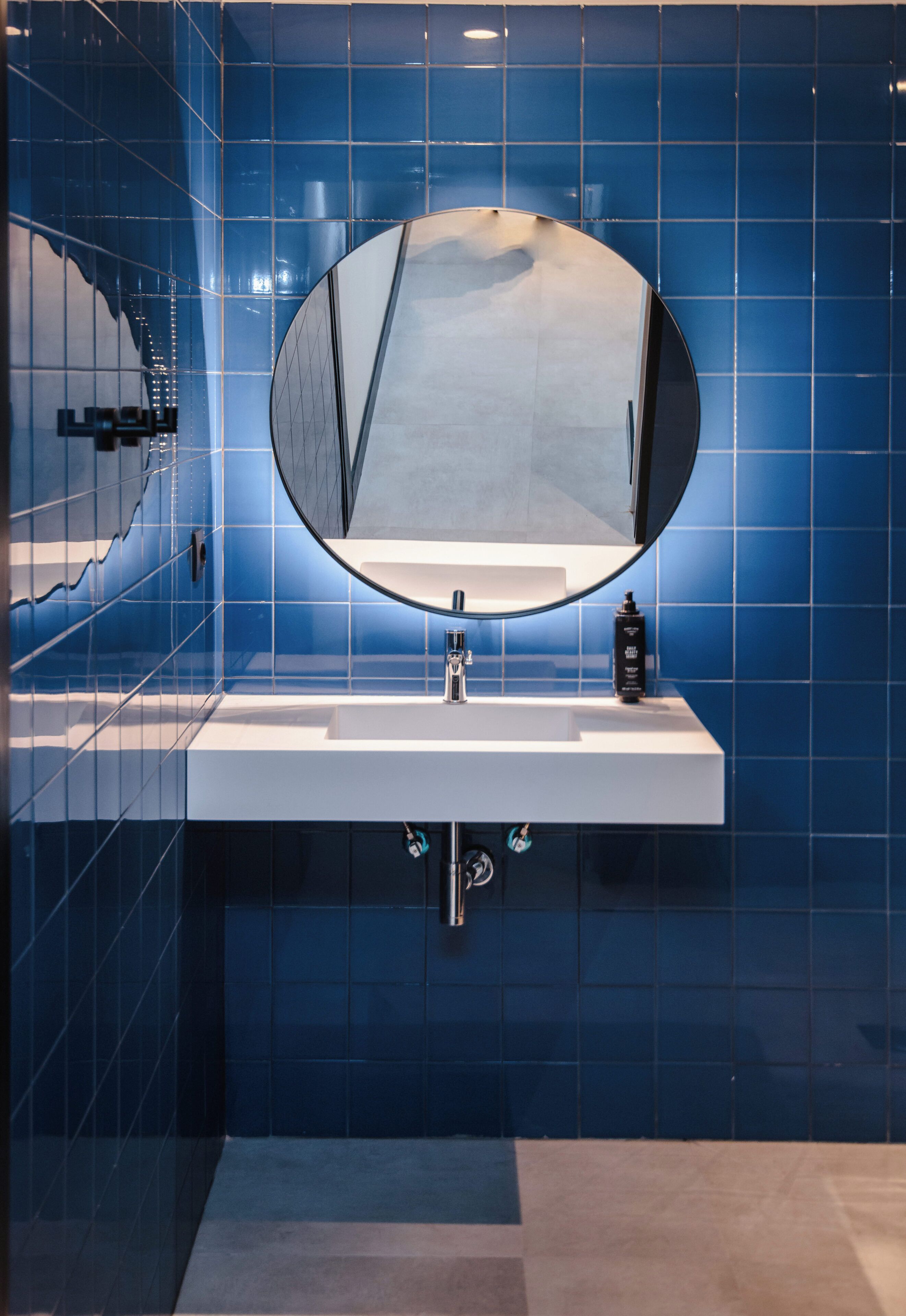Un baño con un lavamanos blanco, un espejo redondo y paredes con azulejos azules.