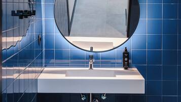 Un baño con un lavamanos blanco, un espejo redondo y paredes con azulejos azules.