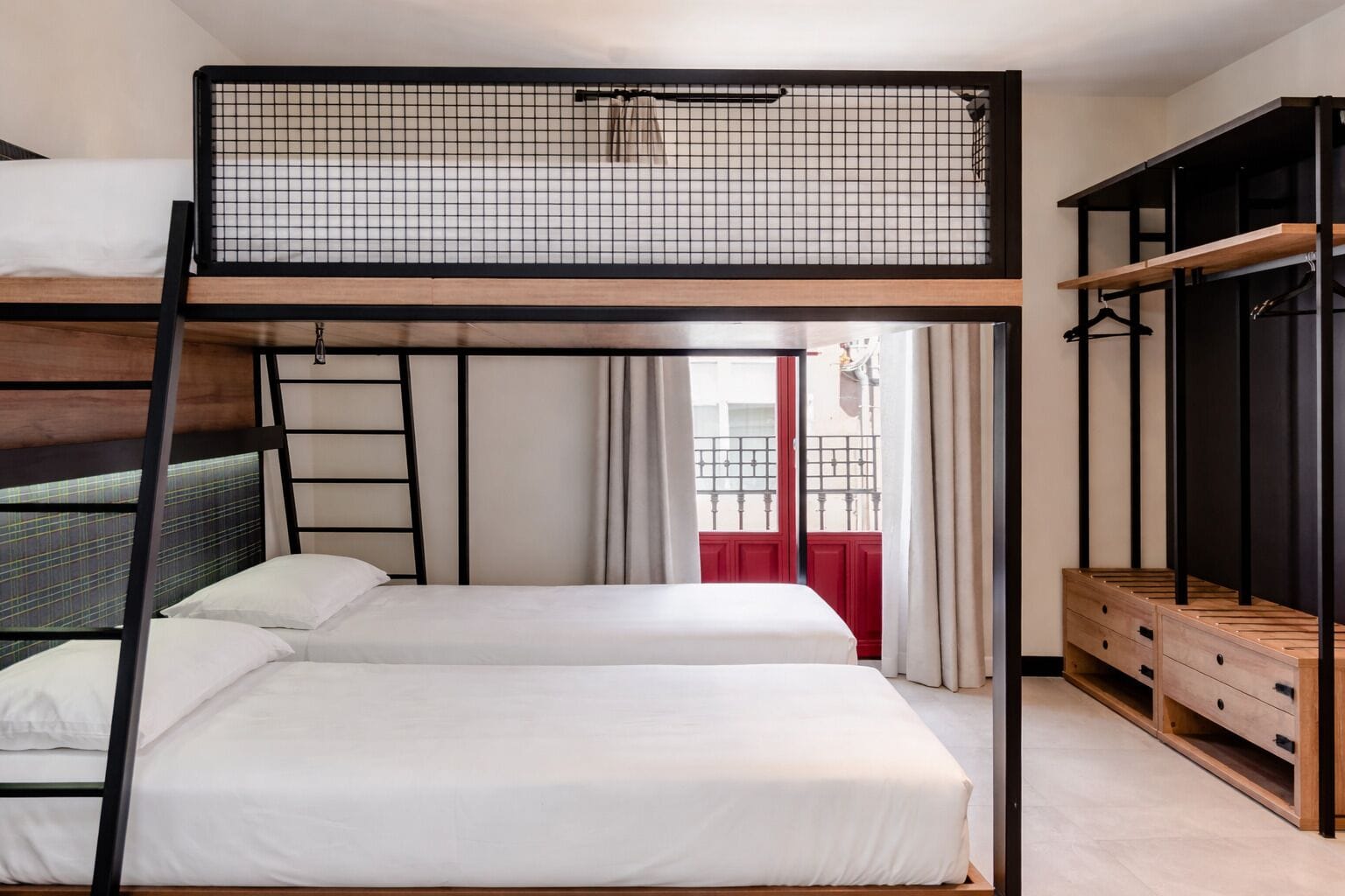 Dormitorio con literas y vista a un edificio rojo a través de una ventana.