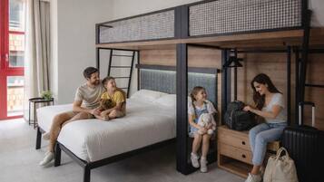 Une chambre avec un lit superposé, une fenêtre, une petite table et une valise.