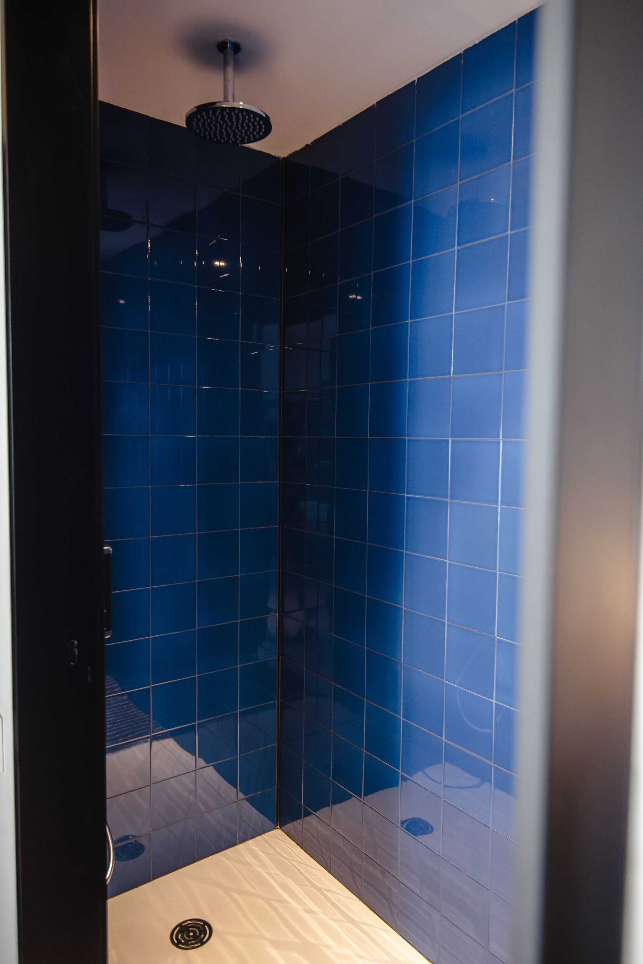 A modern bathroom with blue-tiled walls, a wooden floor, and a ceiling-mounted shower head.