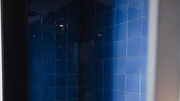 Uma casa de banho moderna com azulejos azuis, chão em madeira e um chuveiro no teto.