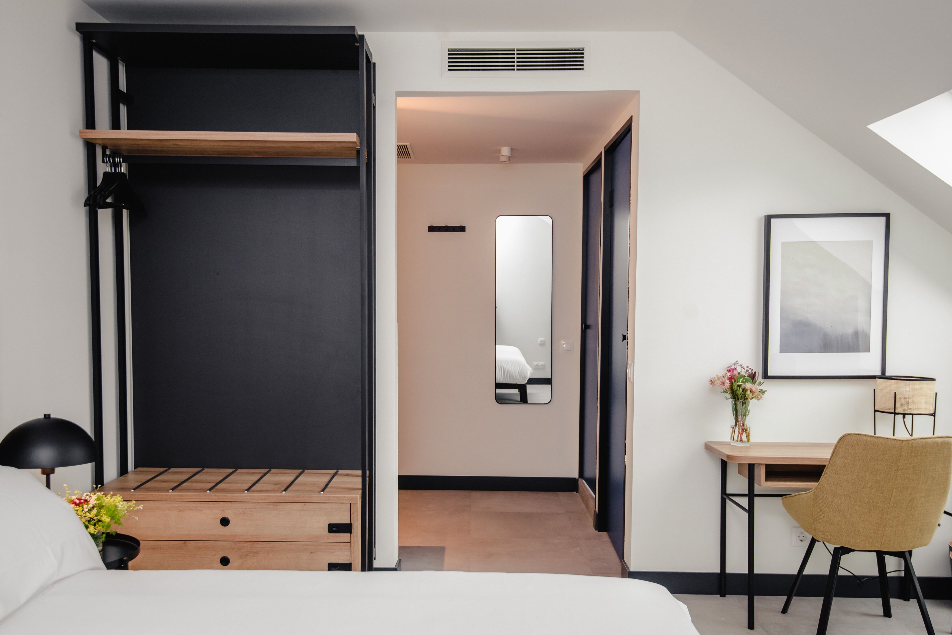 Een moderne hotelkamer met een bed, een bureau, een stoel, een spiegel en een lijst met een foto aan de muur.