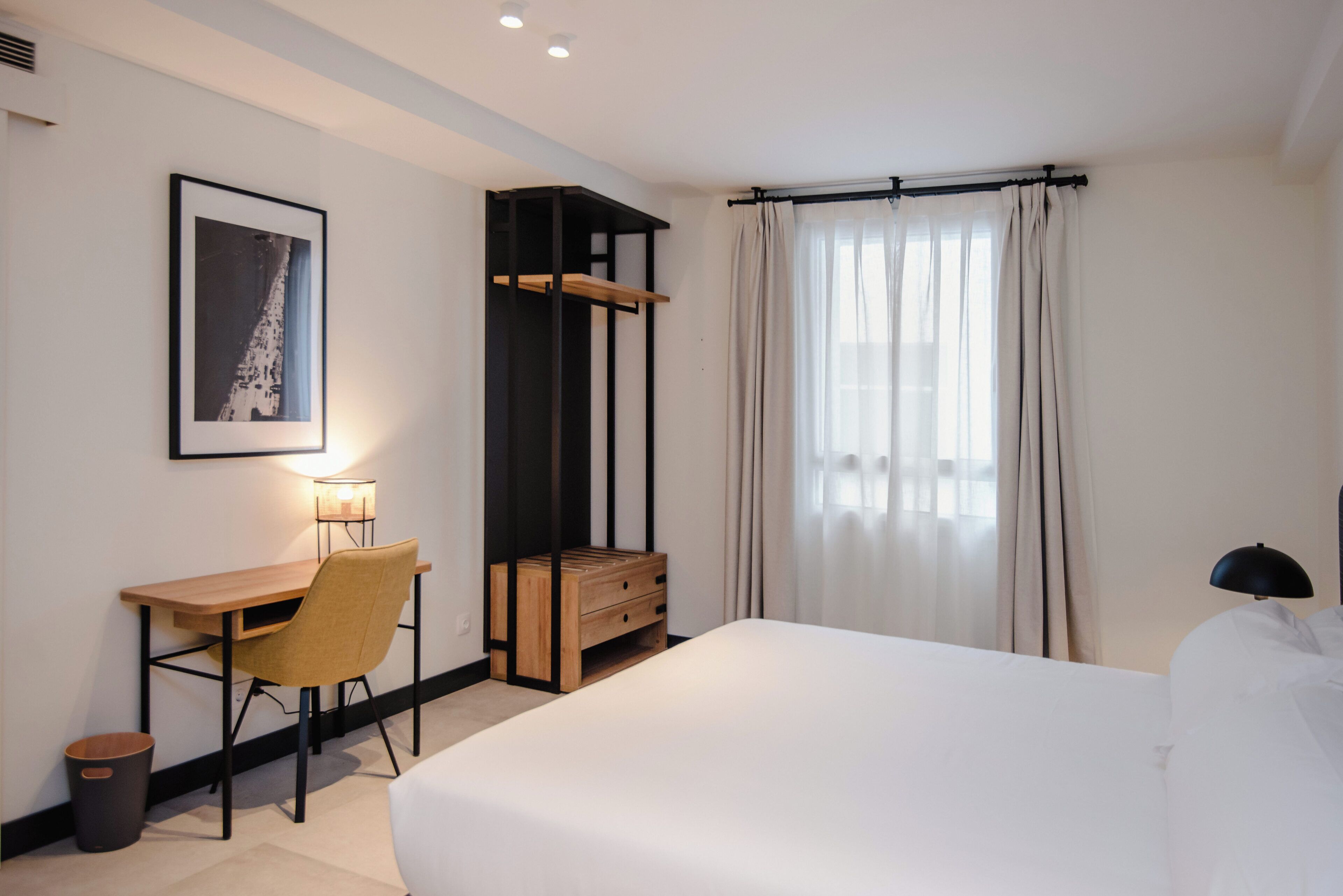 Una habitación de hotel con cama, escritorio, silla y un armario pequeño.