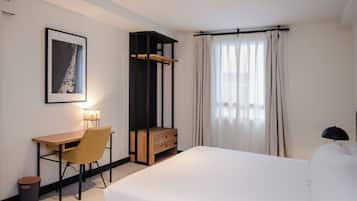 Una habitación de hotel con cama, escritorio, silla y un armario pequeño.