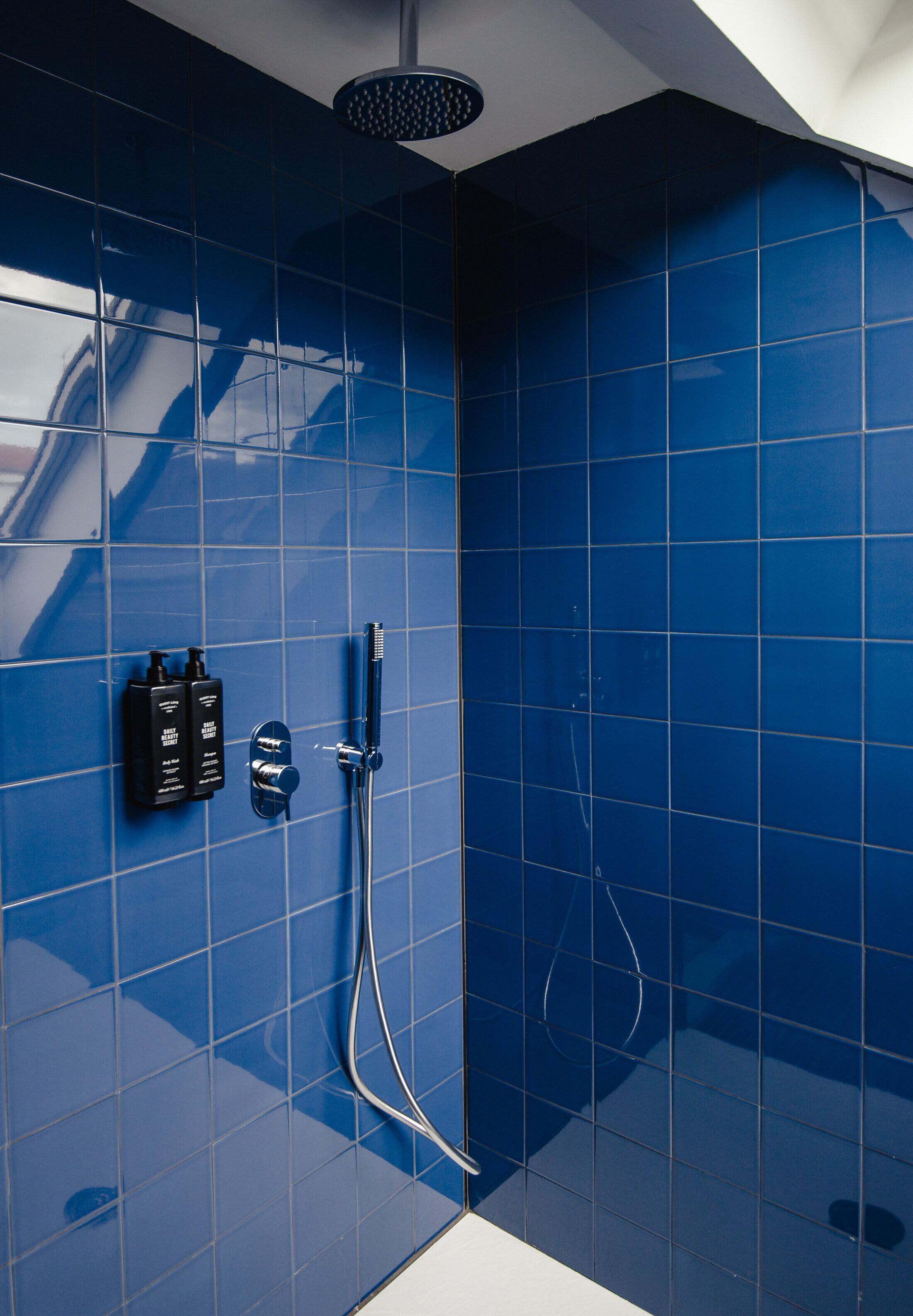 Une salle de bain avec des carreaux bleus, une pomme de douche et deux bouteilles de shampoing.