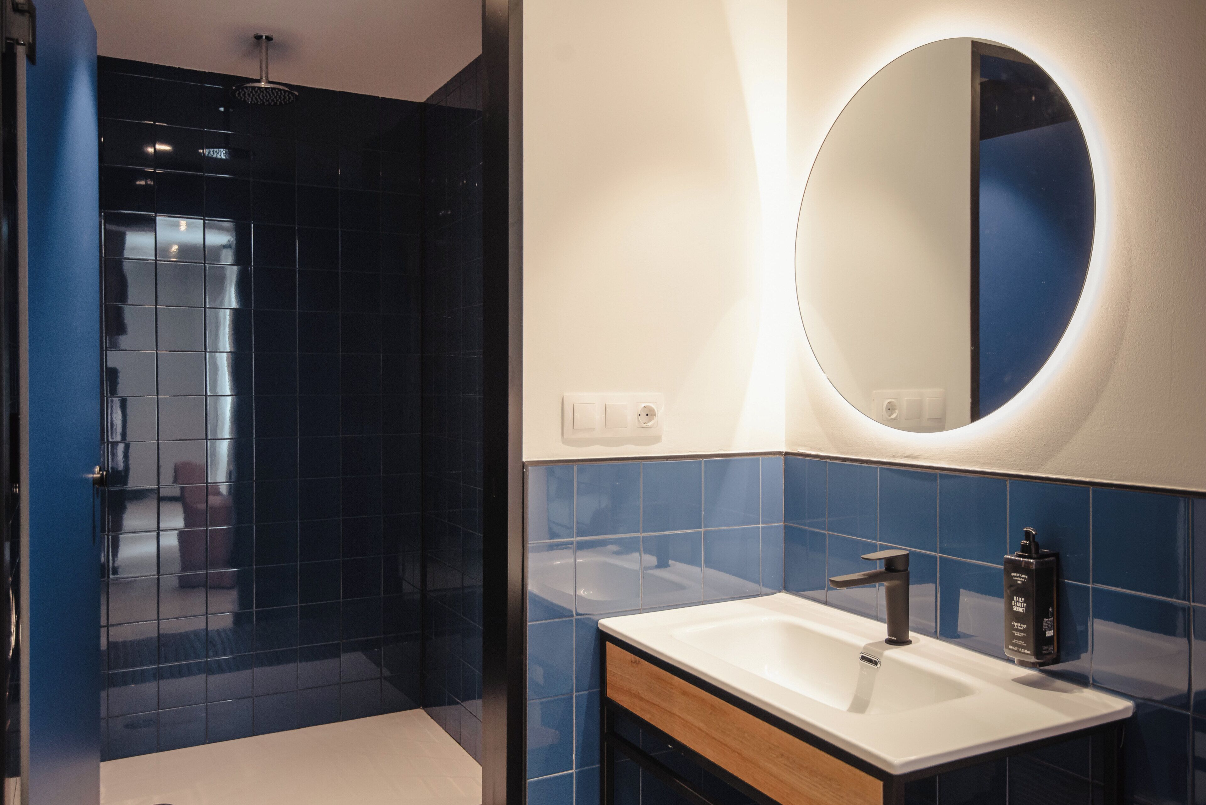 Un baño con diseño moderno, que incluye un espejo grande, un lavamanos y una zona de ducha.