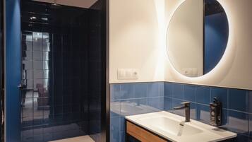 Un baño con diseño moderno, que incluye un espejo grande, un lavamanos y una zona de ducha.