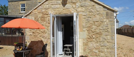 A stone building with a door open, a table with chairs, and an orange umbrella.