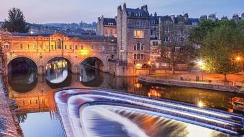 A historic stone bridge with three arches over a calm river, reflecting the surrounding buildings.