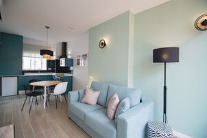 Una sala moderna con un sofá azul claro, una mesa de comedor con sillas y una cocina al fondo.
