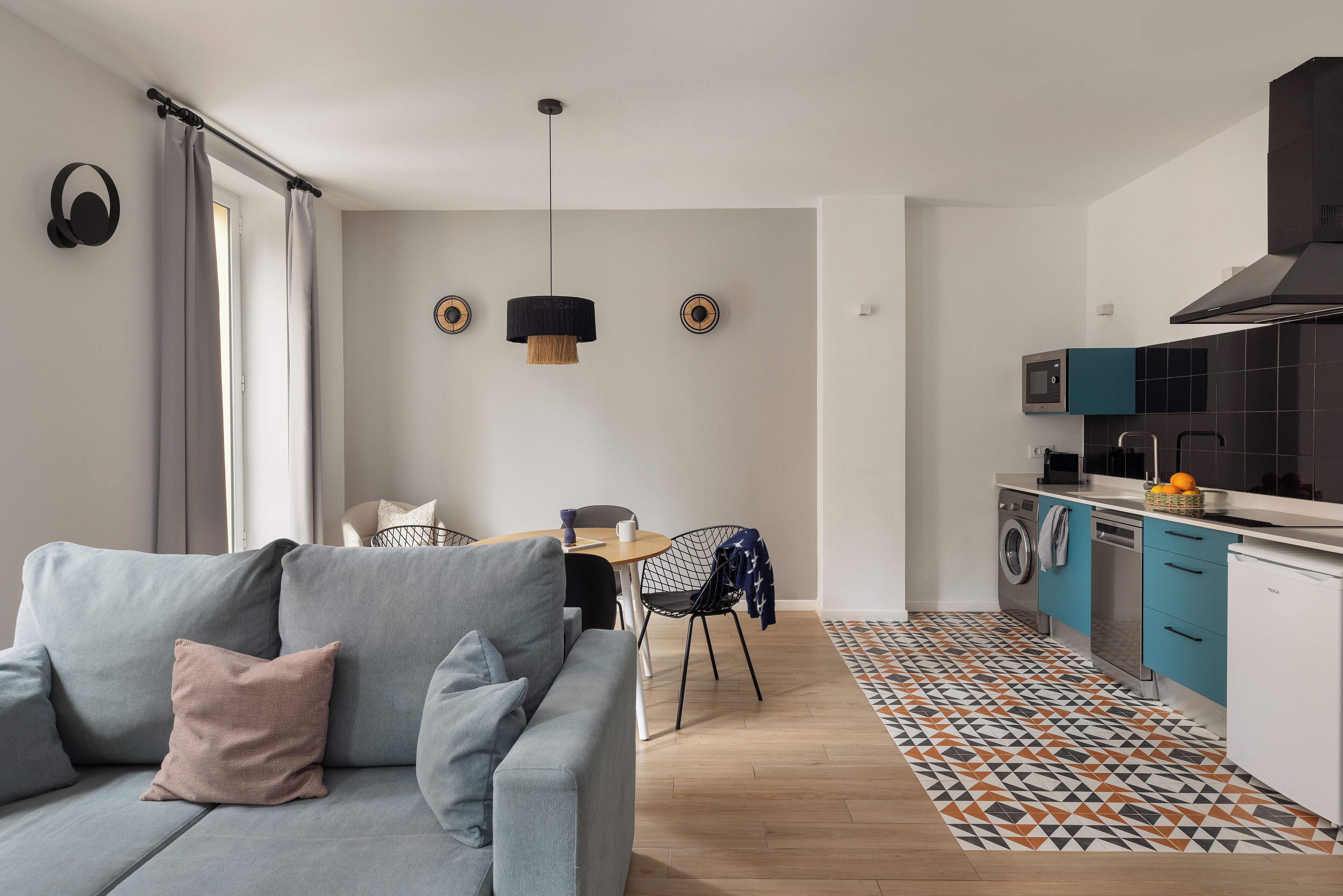 Eine moderne Küche mit Waschmaschine, ein Essbereich mit Tisch und Stühlen sowie ein graues Sofa mit Kissen.
