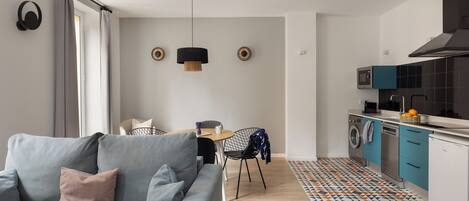 Eine moderne Küche mit Waschmaschine, ein Essbereich mit Tisch und Stühlen sowie ein graues Sofa mit Kissen.