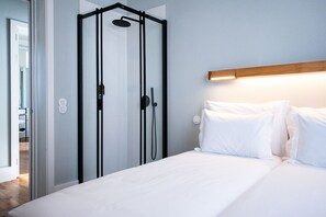 Ett modernt hotellrum med en säng, en duschkabin och en sänggavel i trä.