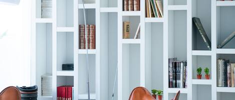 A modern living room with a white bookshelf, leather chairs, and a lamp.