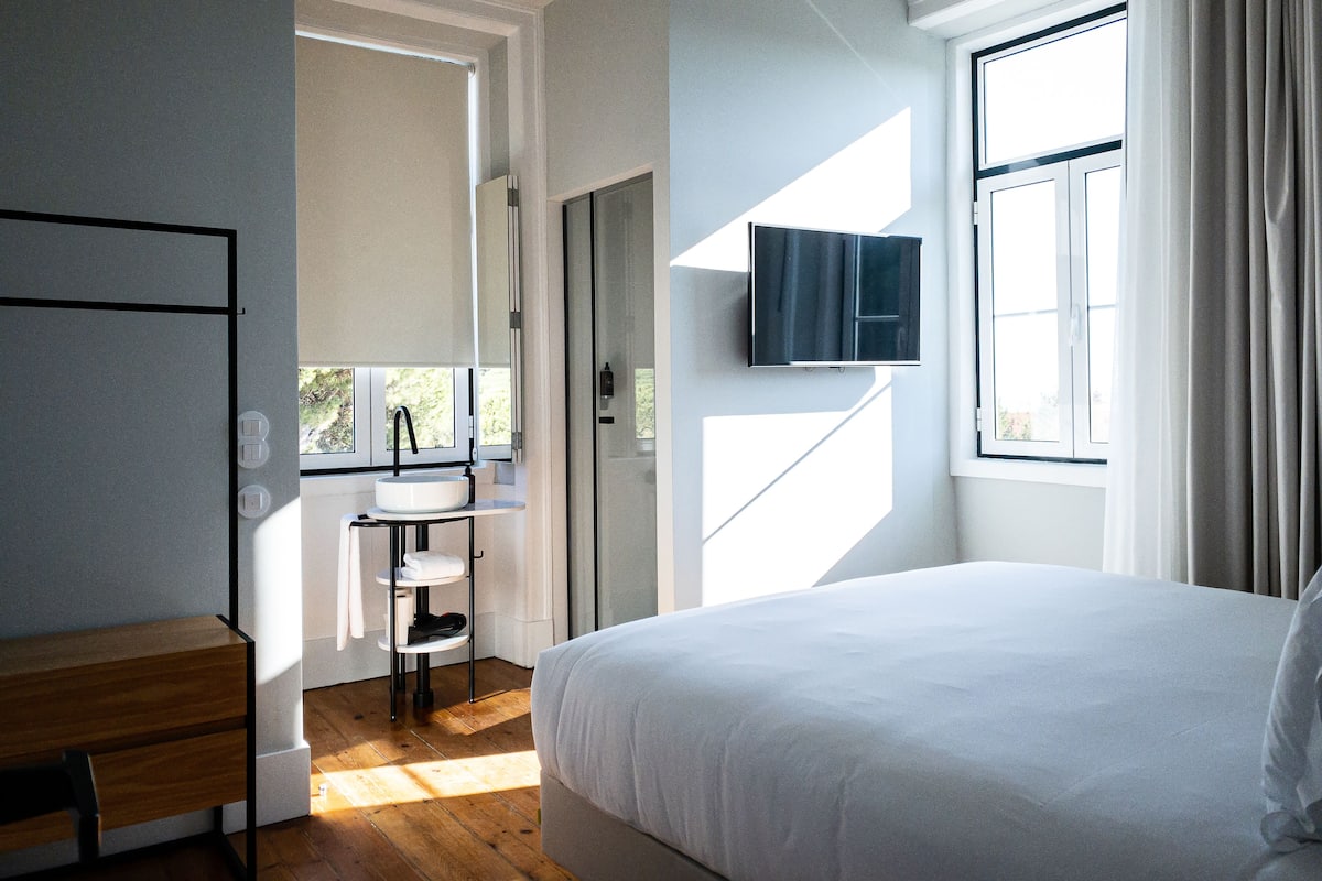 A modern bedroom with a large bed, a bedside table, a built-in TV, and a window with curtains.