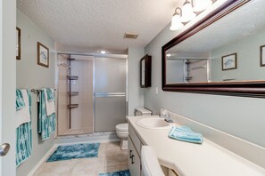 A bathroom with a shower, toilet, sink, and a large mirror.
