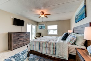 A bedroom with a bed, a ceiling fan, a TV, a dresser, and a painting on the wall. - Oceanfront Sunrise 2 Bed 2 Bath Condo with Pool (Ormond Beach)