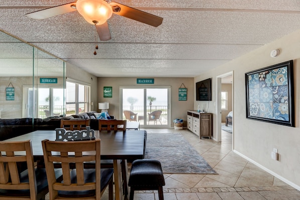 A spacious living area with a dining table, chairs, a ceiling fan, and a view to the outside. - Oceanfront Sunrise 2 Bed 2 Bath Condo with Pool (Ormond Beach)