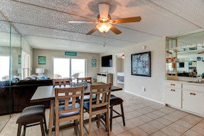 A spacious living area with a dining table, chairs, a ceiling fan, and a kitchen area with cabinets and a countertop. - Oceanfront Sunrise 2 Bed 2 Bath Condo with Pool (Ormond Beach)