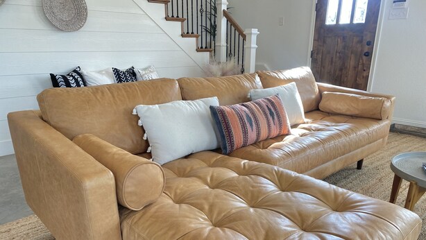A tan leather sofa with a tufted backrest and armrests, accompanied by various patterned cushions. - Close to Baylor & Silos: 3 BR Home Pickleball Court, Ping Pong Table & Barn (Lorena)
