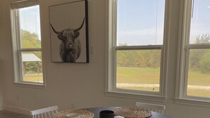 A dining area with a round table, woven placemats, white chairs, and a bull head artwork on the wall. - Close to Baylor & Silos: 3 BR Home Pickleball Court, Ping Pong Table & Barn (Lorena)