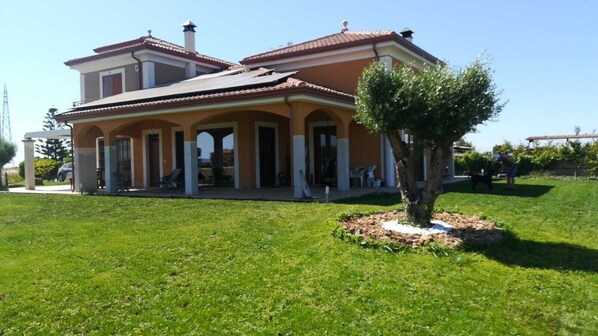 A two-story house with a covered patio and a small tree in the front yard.