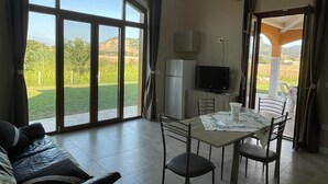 Une pièce spacieuse dotée d’une grande porte-fenêtre coulissante donnant sur un balcon, d’un coin repas avec une table et des chaises, d’un canapé, d’une télévision et d’un réfrigérateur.