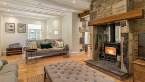Una sala de estar acogedora con chimenea de piedra, un sofá y un otomán grande.