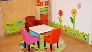 A children's playroom with a wooden floor, a white table, and colorful chairs.
