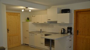 A compact kitchen with white cabinets, a dishwasher, a coffee maker, and a wooden door.